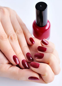 Image of woman's nails with red polish. Article covers why the stress of living through the pandemic is causing weak, peeling and brittle fingernails. Nailcarehq.com