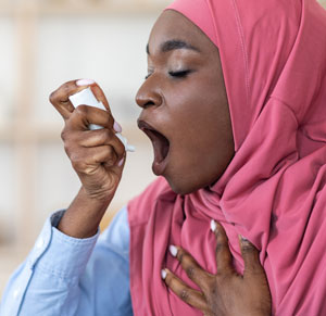 Image of woman struggling to breathe using inhaler. Article covers why the stress of living through the pandemic is causing weak, peeling and brittle fingernails. Nailcarehq.com