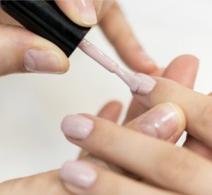 Photo of pale pink nail polish being applied to a woman's fingernails. Nail polish can provide temporary strength and prevent water absorption damage to the nail plate. Nailcarehq.com